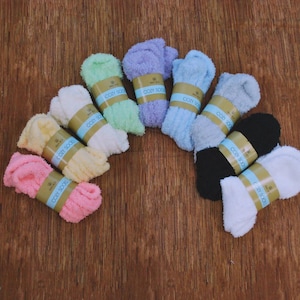 May include: A collection of cozy socks in various colors, including pink, yellow, white, green, purple, blue, gray, black, and white. Each pair is wrapped with a band that reads "COZY SOCKS". The socks are arranged on a wooden surface.