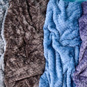 Plush textured throw blanket with a soft rosette pattern, available in dove grey, campfire, ash blue, or lilac — one color included per order.