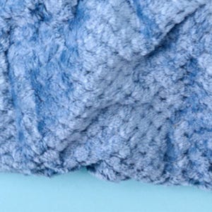 Close-up of plush textured throw blanket fabric in ash blue, showing the soft rosette pattern.