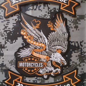Könnte beinhalten: Ein schwarzes besticktes Aufnäher-Set mit einem Adler mit ausgebreiteten Flügeln, orangefarbenen und weißen Akzenten sowie dem Text Live To Ride, Ride Free, Motorcycles und Ride To Live. Das Design enthält Sterne und Banner auf schwarzem Grund.