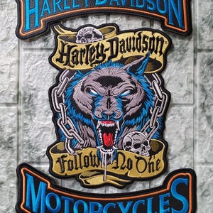 Könnte beinhalten: Gestickter Harley-Davidson-Aufnäher mit einem knurrenden Wolf in Blau und Grau, Ketten und Totenköpfen. Der Aufnäher enthält das Harley-Davidson-Logo und die Worte "Follow No One" und "Motorcycles."