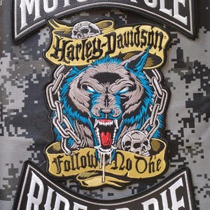 Puede incluir: Un conjunto de tres parches bordados que incluye un arco superior con el texto MOTORCYCLE, un arco inferior con RIDE OR DIE y un emblema central de un lobo gruñendo con pelaje azul, cadenas, calaveras y el texto Harley-Davidson Follow No One.