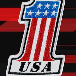 Könnte beinhalten: Gestickter Aufnäher in Form der Zahl Eins, mit den Farben der amerikanischen Flagge. Der obere Teil ist blau mit weißen Sternen, und der untere Teil hat rote und weiße Streifen. Das Wort "USA" steht unten.