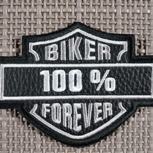 Op de afbeelding: Zwart-witte biker patch met de woorden "BIKER 100% FOREVER" geborduurd. De patch heeft een schildvorm met een getextureerde achtergrond.