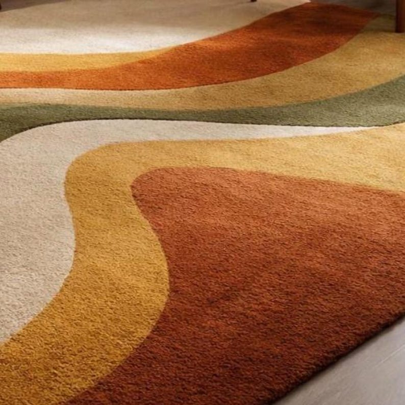 May include: A retro-style area rug with a wavy design in shades of cream, yellow, orange, brown, and green. The rug has a soft, textured appearance, adding warmth and visual interest to a room. The design evokes a vintage aesthetic.