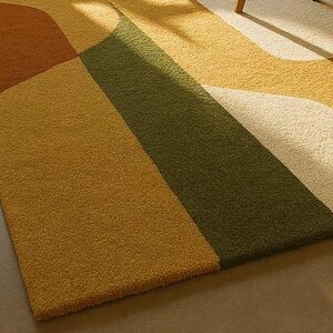 May include: A colorful area rug with a geometric design. The rug features sections of mustard yellow, olive green, brown, and cream colors. The rug has a soft, textured appearance, suggesting a comfortable and inviting feel.