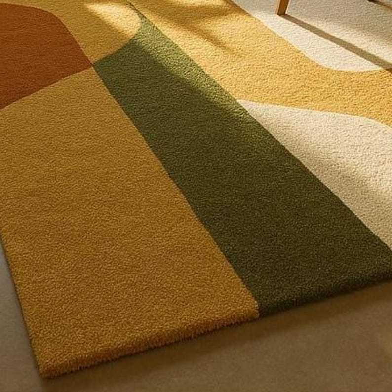 May include: A colorful area rug with a geometric design. The rug features sections of mustard yellow, olive green, brown, and cream colors. The rug has a soft, textured appearance, suggesting a comfortable and inviting feel.