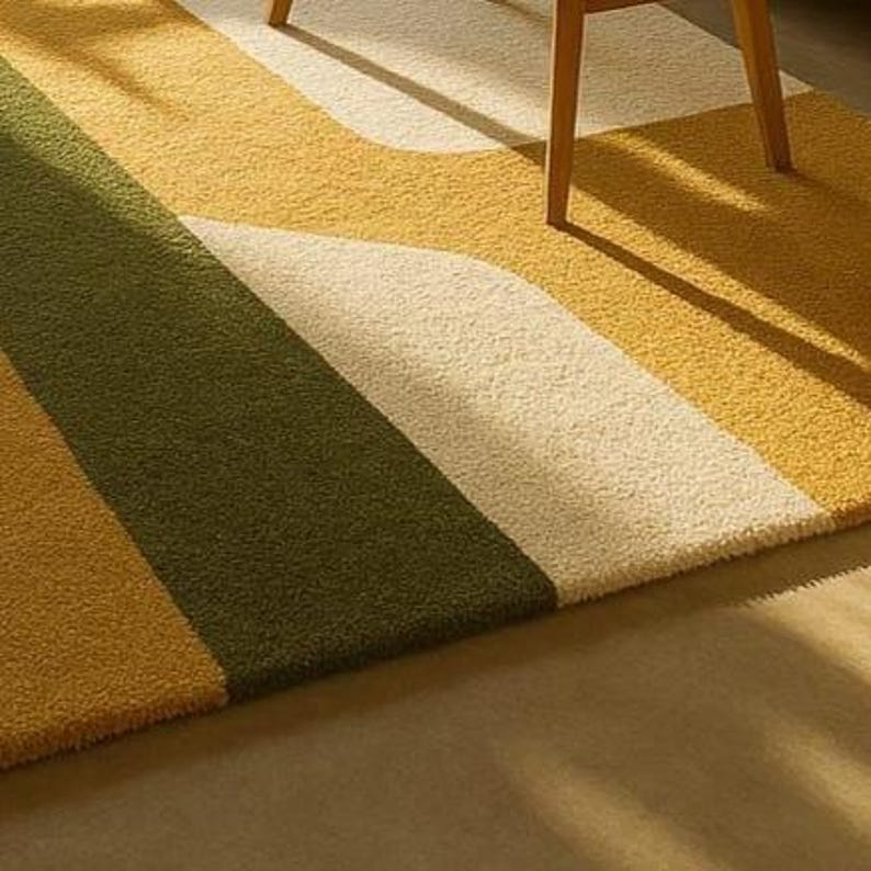 May include: A colorful area rug with a geometric design. The rug features stripes of olive green, cream, and shades of yellow. The rug is made of a soft, textured material and is partially under a wooden chair.