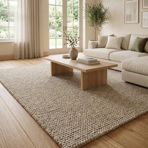 May include: A large, rectangular area rug with a thick, chunky, hand-knitted texture in a neutral beige color. The rug features a prominent, raised loop weave pattern that covers the entire surface, providing a soft and tactile appearance.
