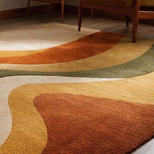 May include: A retro-style area rug with a wavy design in shades of cream, yellow, orange, and green. The rug has a soft, textured appearance and is placed on a wooden floor. The design evokes a vintage aesthetic.