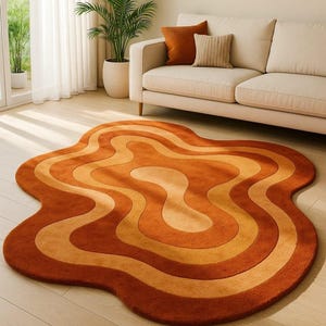May include: An orange and tan area rug with a unique, wavy design. The rug features concentric, organic shapes in varying shades of orange and tan. The rug is placed on a light-colored wooden floor, with a sofa and plants in the background.