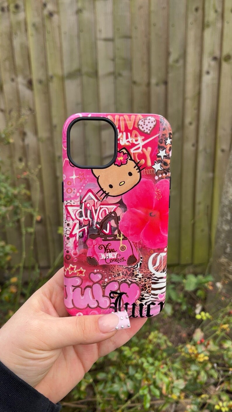 May include: Pink phone case with a collage design featuring a Hello Kitty graphic, a pink flower, and the words "Juicy Couture". The case has a glossy finish and a black camera cutout.