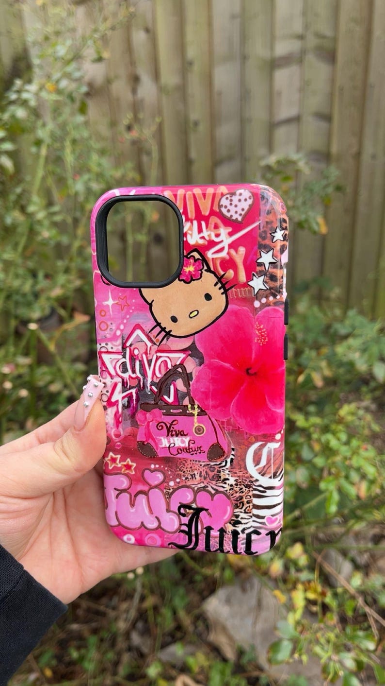 May include: Pink phone case with a vibrant design featuring a Hello Kitty character, a large pink hibiscus flower, and the word "Juicy" in a cursive font. The case has a glossy finish and a black camera cutout.