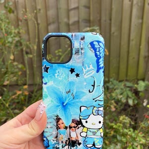 K&ouml;nnte beinhalten: Eine blaue Handyh&uuml;lle mit floralem Design, Sternen und einem Schmetterling. Die H&uuml;lle hat ein Cartoon-Bild von Hello Kitty und Bratz-Puppen. Die H&uuml;lle wird in einer Hand gehalten.