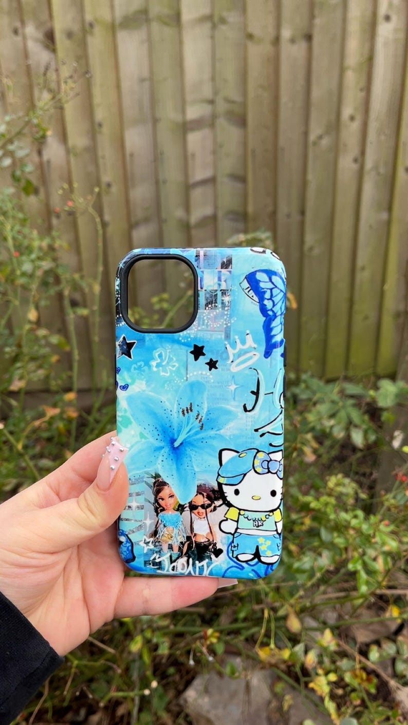 K&ouml;nnte beinhalten: Eine blaue Handyh&uuml;lle mit floralem Design, Sternen und einem Schmetterling. Die H&uuml;lle hat ein Cartoon-Bild von Hello Kitty und Bratz-Puppen. Die H&uuml;lle wird in einer Hand gehalten.