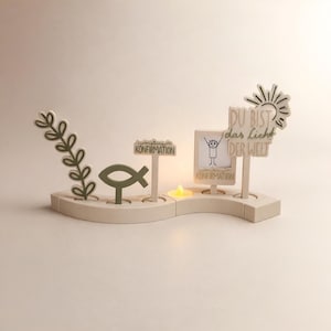 Könnte beinhalten: Ein beigefarbenes Holz-Mittelstück mit einem ausgeschnittenen Fischsymbol, einem Zweig mit Blättern und Schildern mit der Aufschrift "Konfirmation" und "DU BIST das Licht DER WELT". In der Mitte brennt eine kleine Kerze. Das Design ist für eine religiöse Feier.