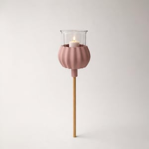 Könnte beinhalten: Ein rosa Kerzenhalter mit Glasaufsatz und Holzstiel. Der Kerzenhalter hat ein bauchiges, geripptes Design und hält eine brennende weiße Kerze. Der Holzstiel ist an der Unterseite des Kerzenhalters befestigt.