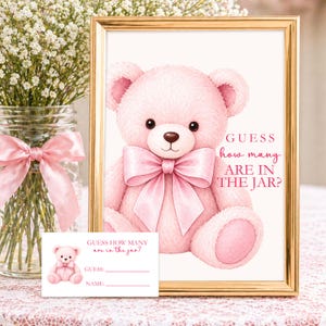 Op de afbeelding: Een roze teddybeerprint in een gouden lijst, met een bijpassende kaart. De beer heeft een grote strik en de tekst "GUESS how many ARE IN THE JAR?" wordt weergegeven. Een vaas met witte bloemen en een roze strik staan op de achtergrond.