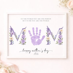 Puede incluir: Una impresión enmarcada con la palabra "MOM" en letras florales lavanda, una huella de mano y el texto "Happy Mother's Day 2026". El texto superior dice "Para el mundo eres una persona, pero para mí eres el mundo".