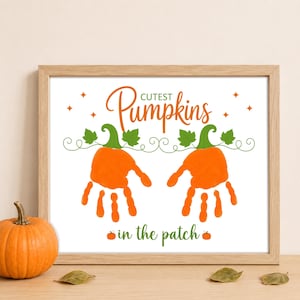 Peut inclure: Une impression encadrée avec le texte Cutest Pumpkins in the patch, deux empreintes de mains orange en forme de citrouilles, des tiges et feuilles vertes, et des étoiles orange sur fond blanc dans un cadre en bois clair.