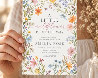 Puede incluir: Una tarjeta de invitación rectangular blanca con un borde floral de acuarela con flores silvestres rosas, naranjas, amarillas y azules. El texto dice: A LITTLE wildflower IS ON THE WAY, PLEASE JOIN US FOR A BABY SHOWER TO CELEBRATE AMELIA ROSE.