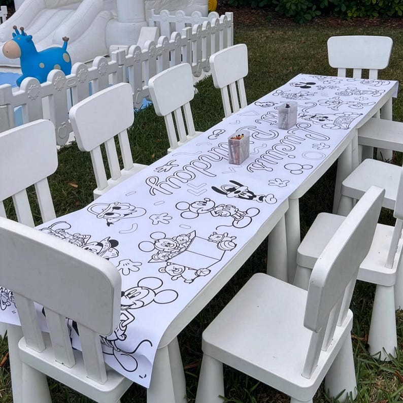 Puede incluir: Un juego de mesa y sillas blancas para una fiesta infantil. La mesa est&aacute; cubierta con un mantel de papel blanco con personajes de dibujos animados en blanco y negro y las palabras "Happy Birthday Lucia".