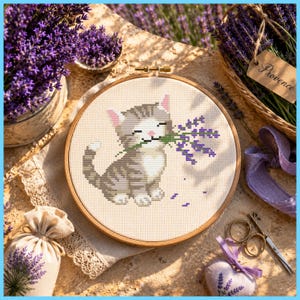 Peut inclure: Un tambour à broder circulaire en bois contenant un motif au point de croix représentant un chat tigré gris tenant un brin de lavande violette dans sa gueule. Le chat a des pattes et un poitrail blancs sur un tissu de couleur crème.