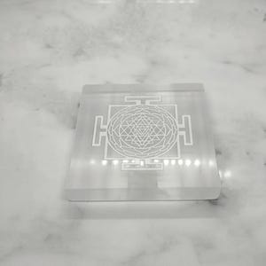 Natural white selenite grid featuring an intricate central Shri Yantra symbol surrounded by sacred geometric elements.