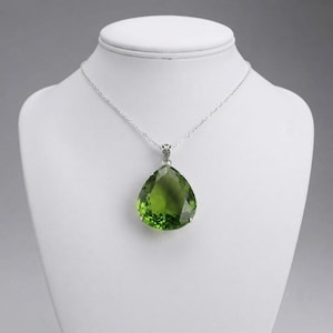 Closeup of large pear-shaped green emerald gemstone pendant with silver prongs and bail, handmade statement necklace