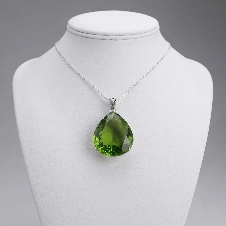 Closeup of large pear-shaped green emerald gemstone pendant with silver prongs and bail, handmade statement necklace