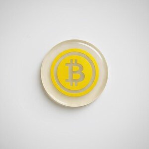 Close-up detail shot of the smooth epoxy resin edge and metallic yellow Bitcoin logo embedded inside the physical coin token.