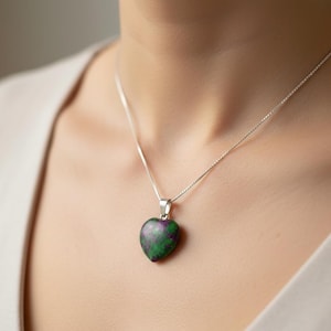 Könnte beinhalten: Halskette mit herzförmigem Anhänger und Silberkette. Der Anhänger besteht aus einem grünen und violetten Stein. Die Halskette wird um den Hals getragen.