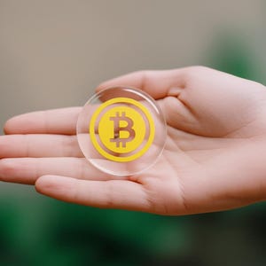 Handmade 2-inch clear resin Bitcoin medallion styled on a dark notebook with a sleek pen for office desk decor.