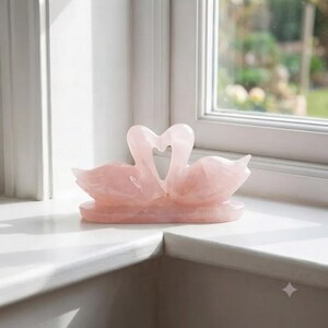 Close-up view of a hand-carved rose quartz love birds crystal sculpture showing smooth polished natural pink gemstone details.