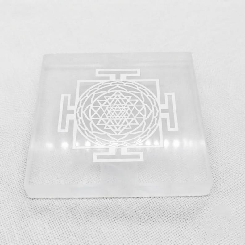 Close-up of Shri Yantra sacred geometry engraving on a polished translucent white selenite crystal charging plate.