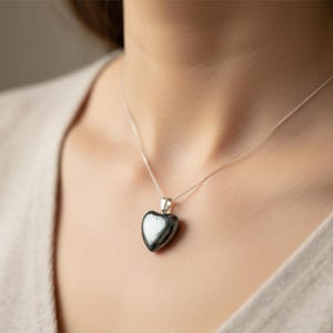 May include: A silver necklace with a heart-shaped pendant. The pendant is a dark, glossy gray color. The necklace is worn around the neck.