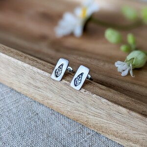 May include: A pair of silver earrings featuring a leaf design. The earrings are rectangular in shape and have a simple, minimalist style.