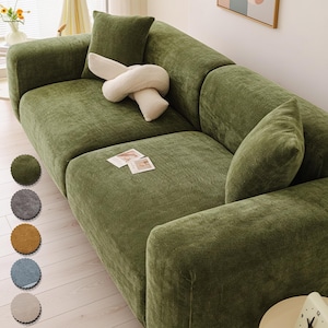 May include: A large, olive green sectional sofa with a corduroy texture. The sofa has several cushions and a decorative white knot-shaped pillow. A small, square pillow matches the sofa's color. Several color swatches are displayed on the left.