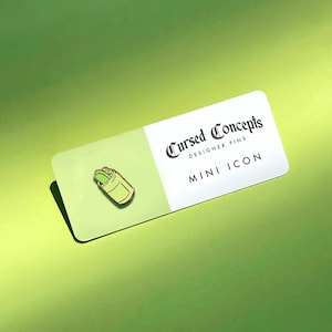 Può includere: Uno spillo in smalto verde e giallo che rappresenta una lattina di cibo con un cetriolo verde all'interno. Lo spillo è su una carta bianca con il testo "Cursed Concepts Designer Pins Mini Icon".