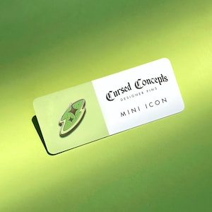 Könnte beinhalten: Eine grüne und braune Emaille-Anstecknadel mit einem Cartoon-Bild eines geteilten Avocados mit einem Kern. Die Anstecknadel befindet sich auf einer weißen Karte mit dem Text "Cursed Concepts Designer Pins Mini Icon".