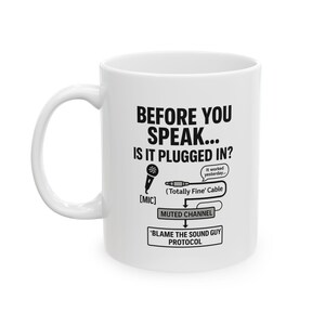 Puede incluir: Taza de cerámica blanca con un gráfico negro que dice "BEFORE YOU SPEAK... IS IT PLUGGED IN?" con un micrófono, un cable y texto sobre el protocolo del técnico de sonido. La taza tiene un asa blanca.