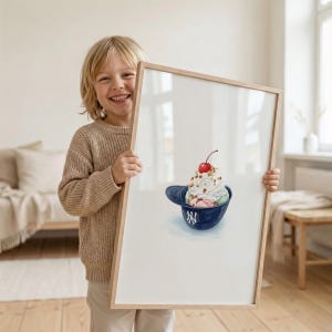 May include: A framed watercolor print featuring a baseball cap filled with ice cream, topped with a cherry and nuts. The cap is navy blue with a white "NY" logo. The artwork is displayed in a light wood frame.
