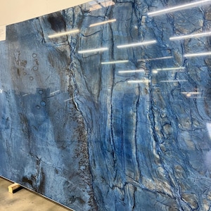 May include: A large, polished slab of blue stone featuring a complex, natural pattern of deep navy and bright azure veins. The surface displays a high-gloss finish with intricate, swirling mineral textures and dark, organic-looking inclusions.