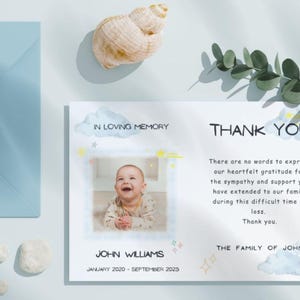May include: A sympathy card with a photo of a baby, text that reads "IN LOVING MEMORY" and "THANK YOU". The card includes the name "JOHN WILLIAMS" and dates "JANUARY 2020 - SEPTEMBER 2025". A blue envelope and a seashell are also visible.