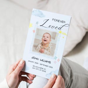 May include: A memorial card held by a person, featuring a smiling baby photo. The card has the words "FOREVER Loved" and the name "JOHN WILLIAMS" with dates and an address. Pastel clouds, stars, and diamonds decorate the card.