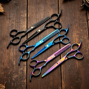 Peut inclure: Trois paires de ciseaux de coiffure disposées en diagonale. Une paire est noir mat, une est bleu métallique et une présente une finition irisée multicolore. Chaque paire comprend une lame dentelée pour effiler et une lame standard.