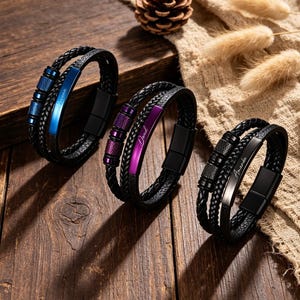 May include: Three black leather bracelets with braided bands and magnetic clasps. Each bracelet features a colored metal plate with a name engraved on it: blue with "Leona", purple with "Daniel", and black with "Amanda".
