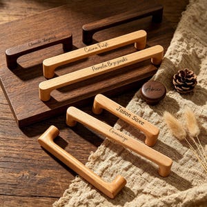 May include: A collection of light and dark wood cabinet handles featuring engraved names including Chanelle Kazymek, Celina Fulst, Pamela Brzezinski, Jason Saxe, and Gramarye, alongside a single round dark wood knob engraved with the name Adrian.