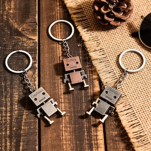 Peut inclure: Trois porte-clés en forme de robot avec des noms personnalisés. Les porte-clés sont en métal argenté et cuivré. Chaque robot a un porte-clés circulaire et une petite chaîne. Les noms "Constance", "Brittany" et "Nicholson" sont gravés sur les têtes des robots.