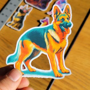 May include: A colorful sticker featuring a stylized German Shepherd dog in a standing pose. The sticker has a vibrant color palette of orange, blue, and yellow. Additional dog-themed stickers are visible in the background.
